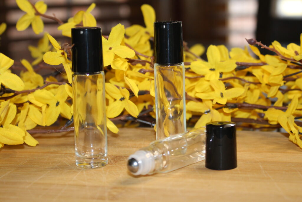 Clear Essential Oil roller bottles on wooden surface with yellow flowers in background