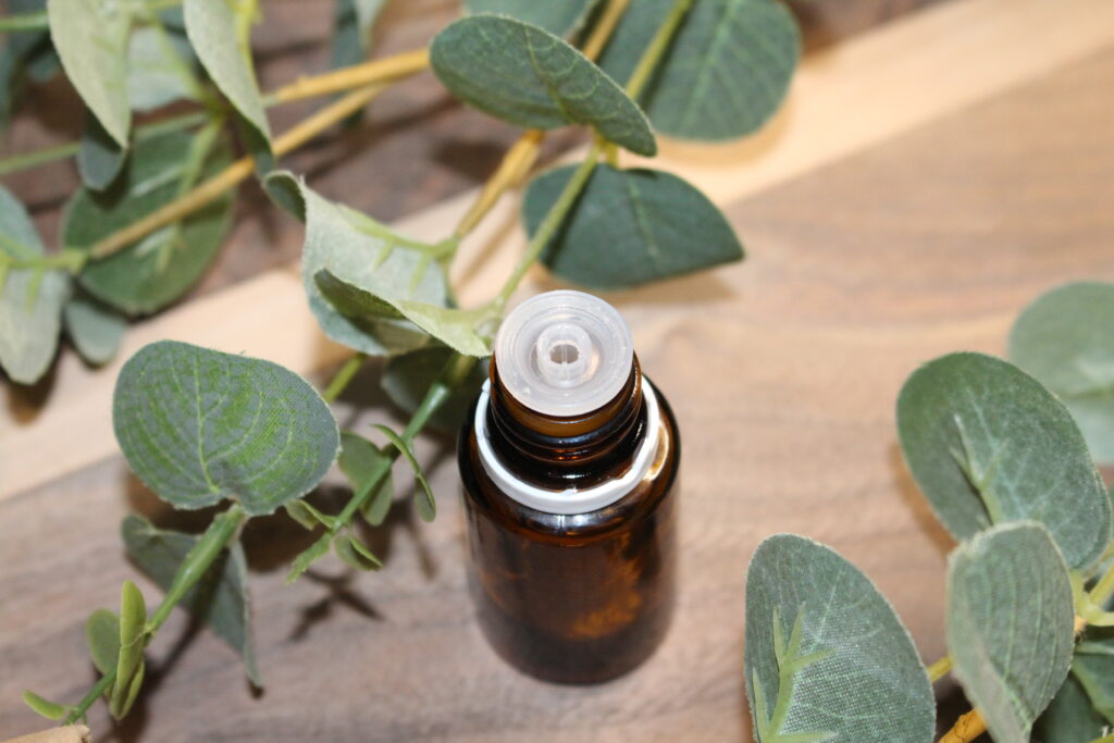 Empty essential oil bottle with greenery on a wooden surface