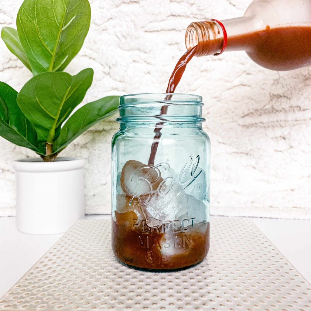 Ningxia Red pour in blue mason jar with ice with plant in the background