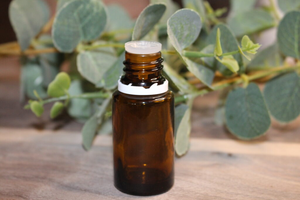 Empty essential oil bottle on wooden cutting board with greenery in the background.