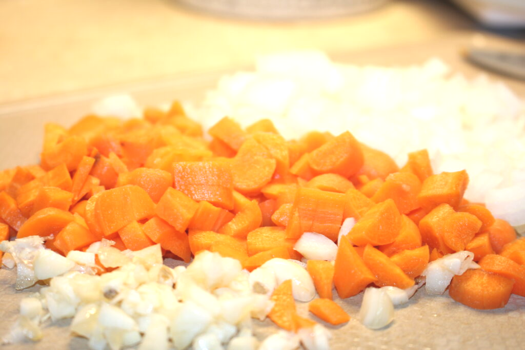 Diced carrots and onions with minced garlic on a tan cutting board