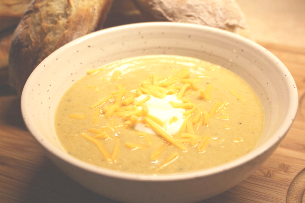 Broccoli Cheddar Soup with shredded cheese and Greek yogurt with baguettes behind on wooden board