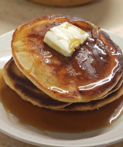 Stack of pancakes with syrup and butter square on a tan plate