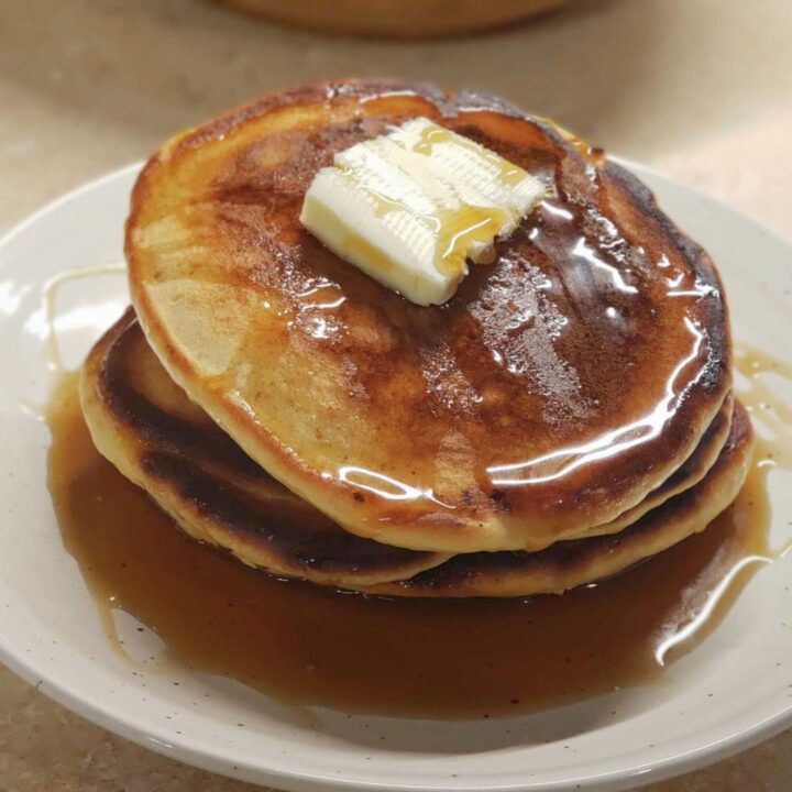 Stack of pancakes with syrup and butter square on a tan plate