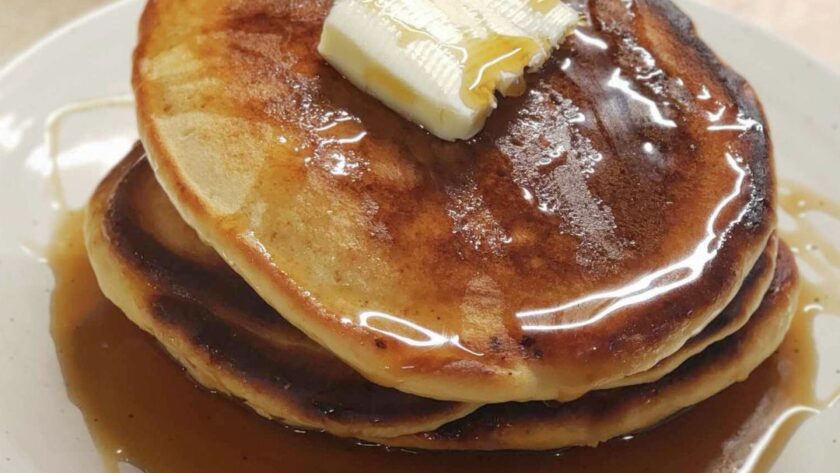 Stack of pancakes with syrup and butter square on a tan plate