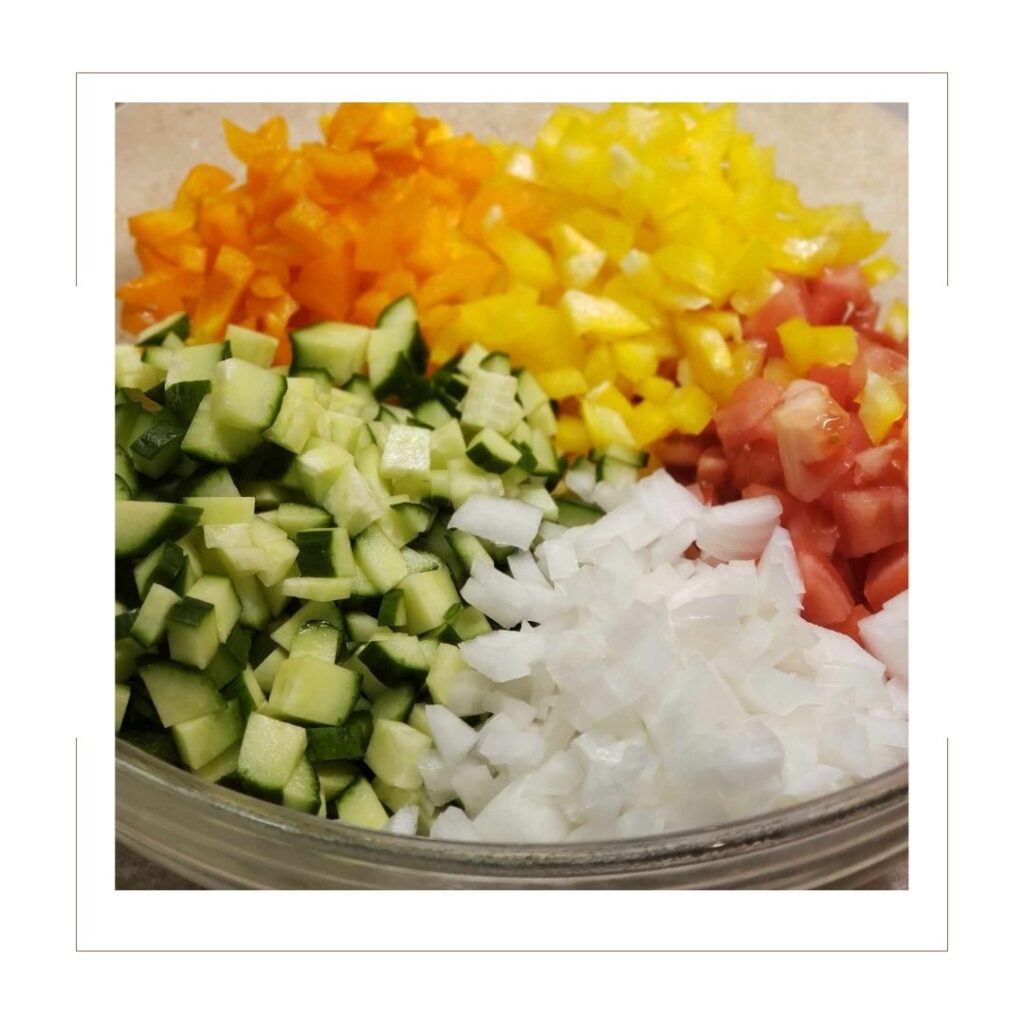 Diced Cucumber, Yellow and Orange Bell Pepper, Roma Tomato and Yellow Onion in a glass bowl.