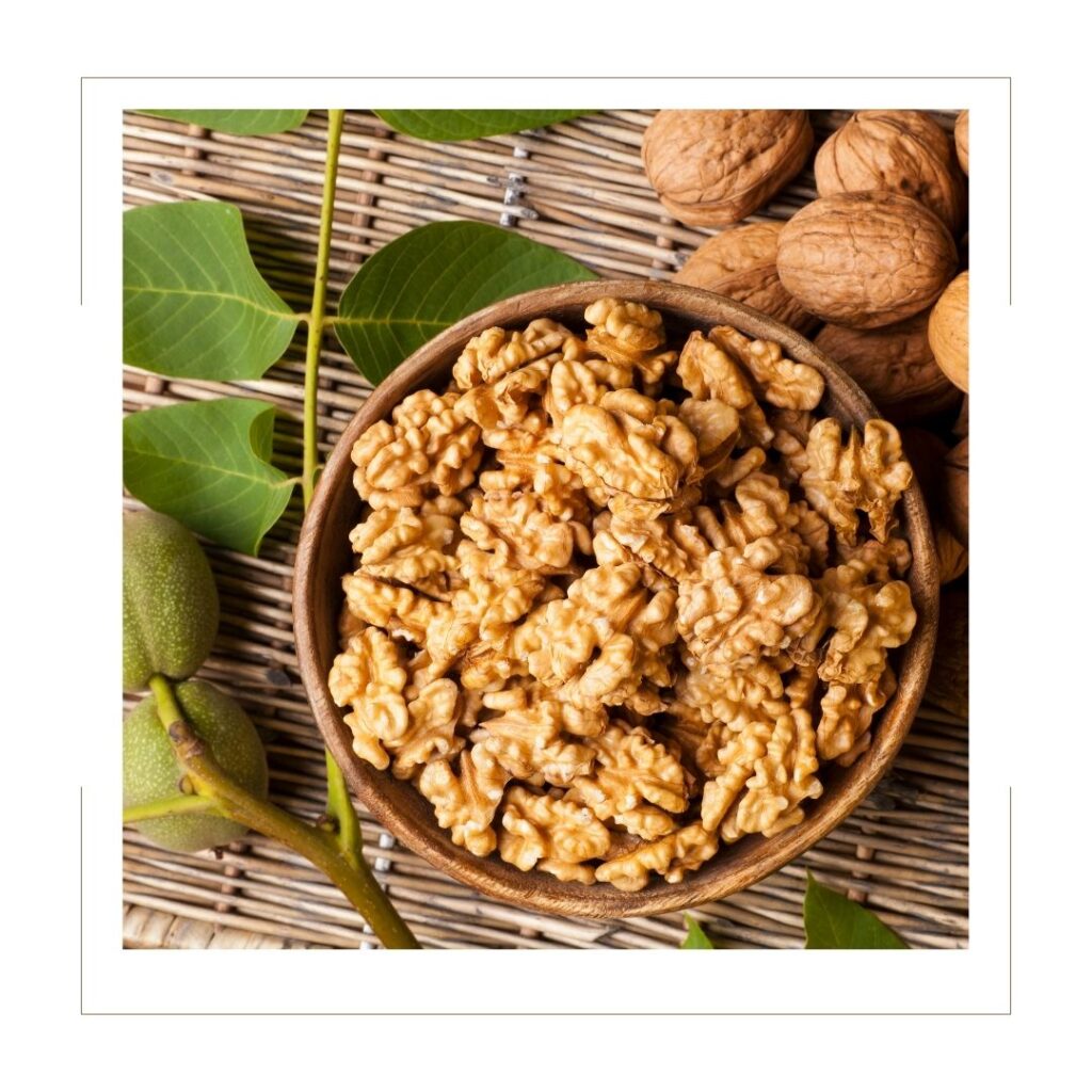 Bowl full of shelled walnuts on a bamboo mat with whole walnuts beside with greenery