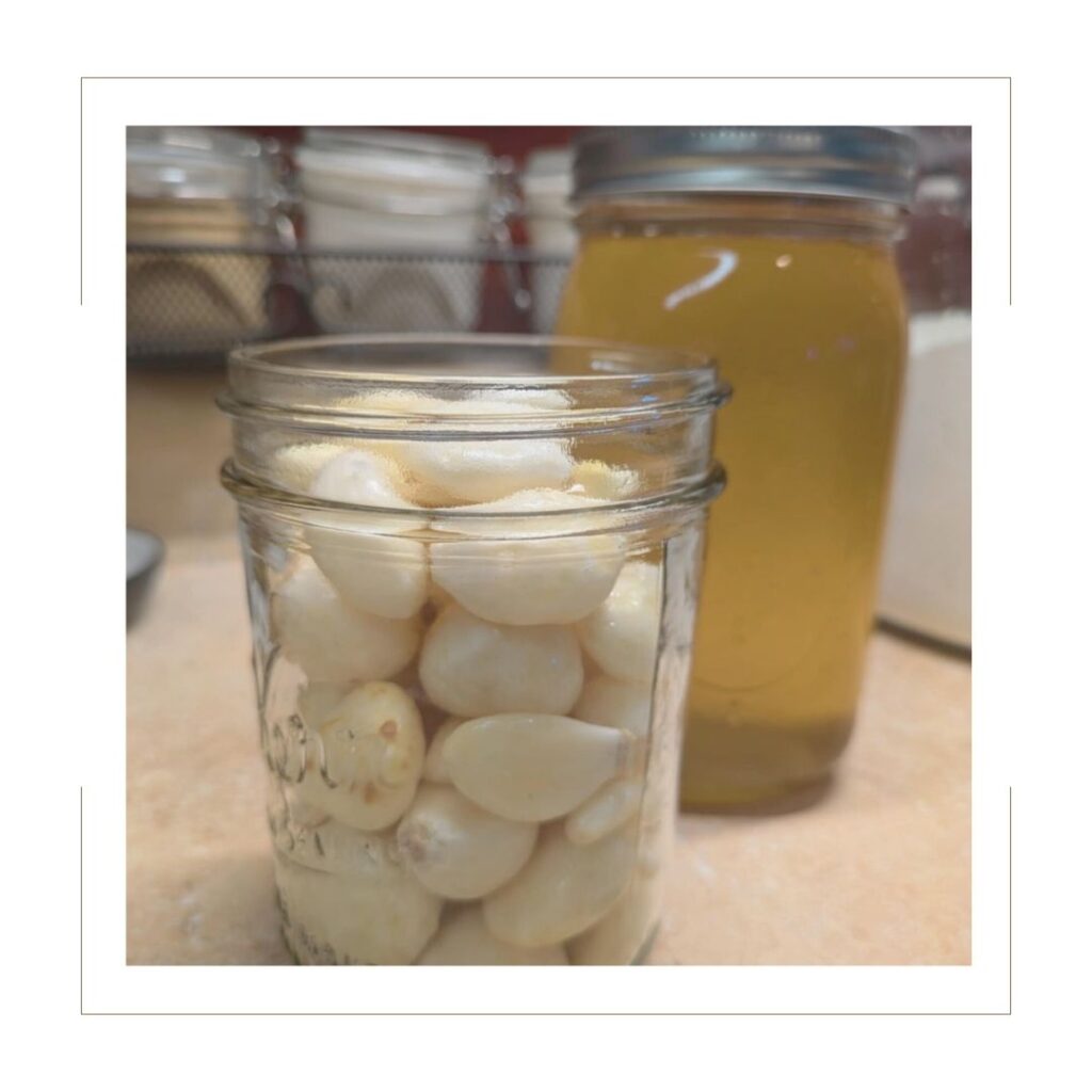 garlic cloves in a mason jar with a jar of honey behind it.