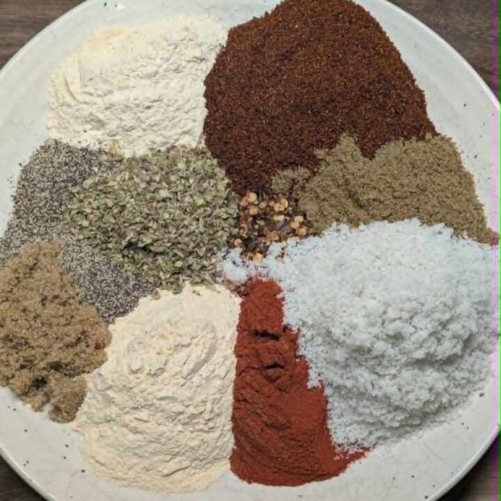 Overhead flat-lay of individual taco seasoning spices arranged on a white plate